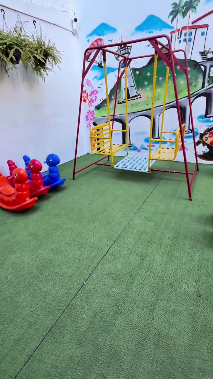 Área externa com balanços e brinquedos sobre piso emborrachado verde